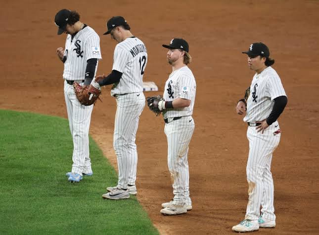 Four White Sox infielders in home pinstripes stand on the infield dirt between plays